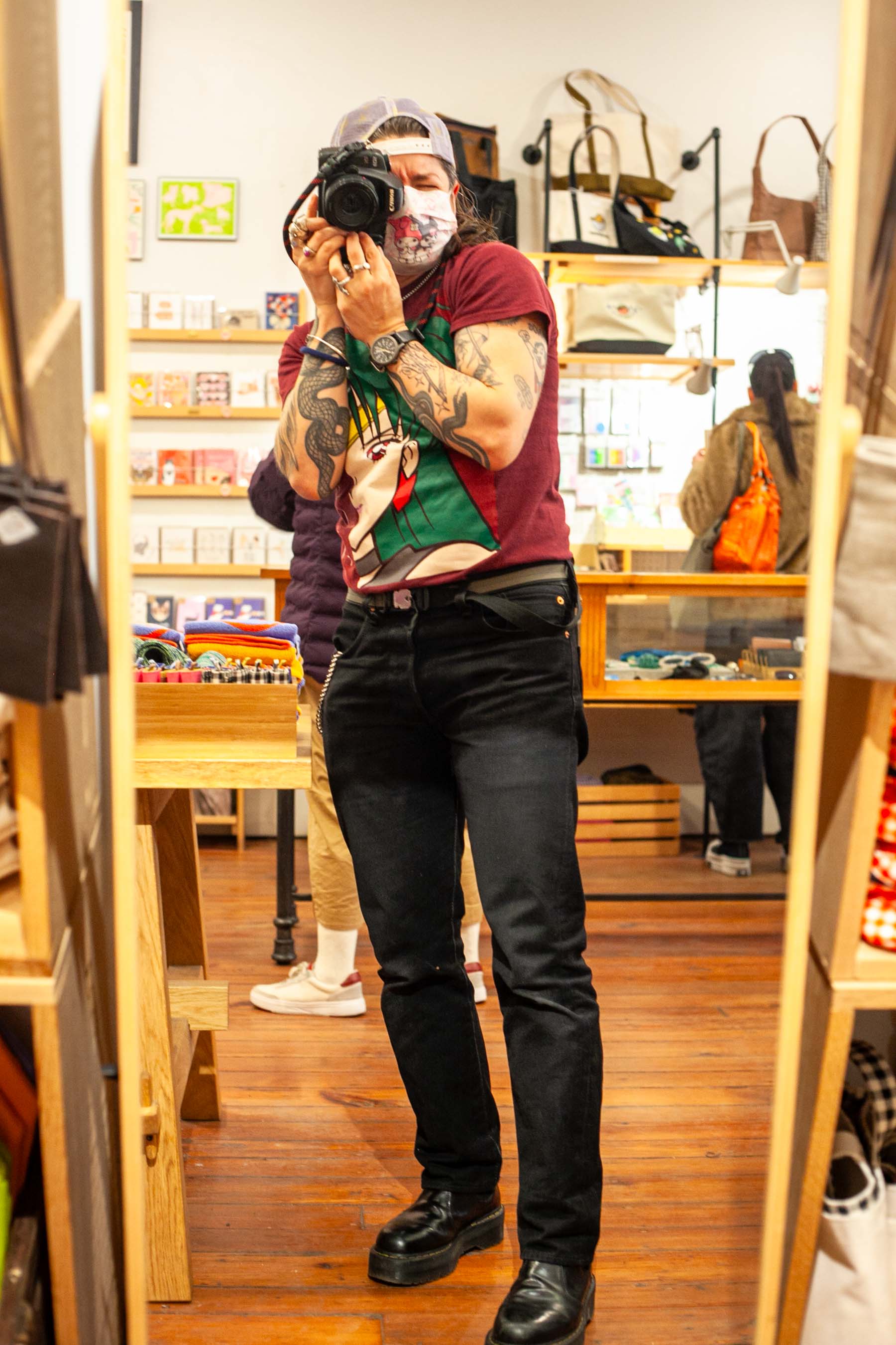 self-portrait photo in a mirror at a client's store, my face obscured by my camera and face mask