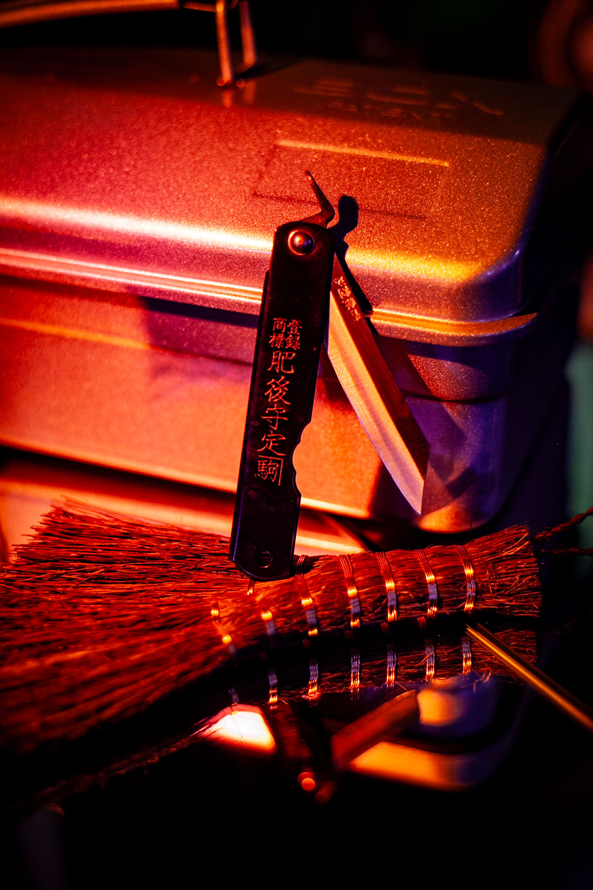 folding knife leaning on straw hand broom and metal toolbox